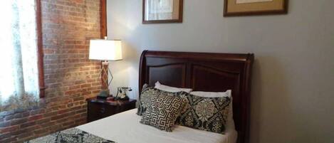 A neatly made bed with patterned pillows, a wooden headboard, and a nightstand with a lamp.