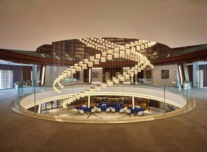 A modern interior with a central spiral staircase, glass railings, and a seating area with sofas and tables. - Le Gray (Beirut)