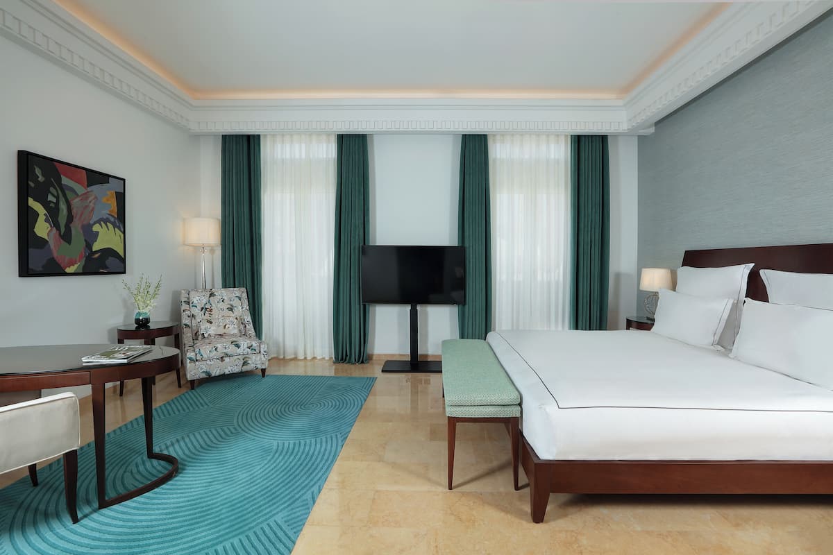 Habitación de hotel con cama, escritorio, silla, televisor y un cuadro en la pared.