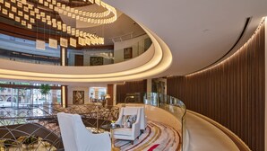A modern interior with a curved staircase, seating area with armchairs, and a view of the outside through large windows. - Le Gray (Beirut)
