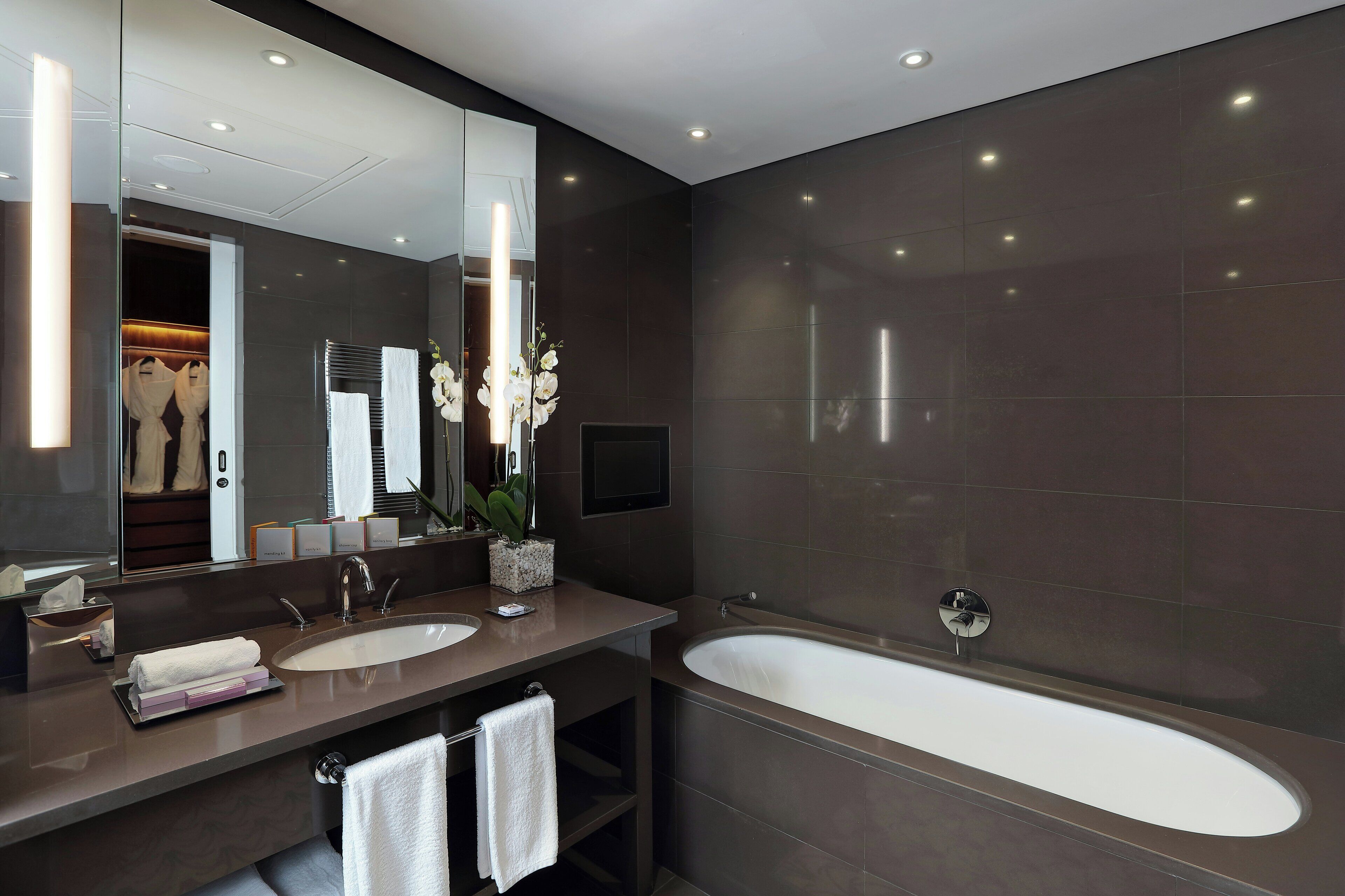 Un baño moderno con un espejo grande, dos lavamanos, una bañera y un mueble de tocador con toallero.