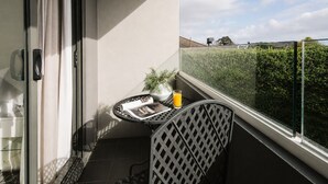 Un balcon avec une petite table, une chaise, un pot de fleurs et un verre de jus d’orange.