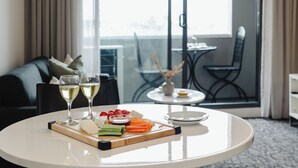 Une table à manger avec une assiette blanche, deux verres de vin blanc, une planche en bois sur laquelle sont disposés du fromage et des légumes, ainsi qu’un petit récipient contenant de la sauce.