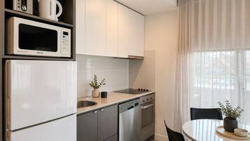 Una cocina moderna con armarios blancos, electrodomésticos de acero inoxidable, una zona de comedor con mesa y sillas, y una ventana con cortinas.