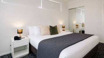 A hotel room with a large bed, bedside lamps, a nightstand, a mirror, and a carpeted floor.