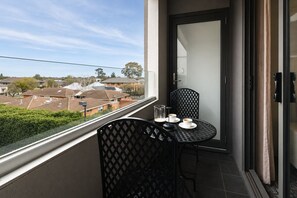 A balcony with a table and chairs, a glass of water, and a cup of coffee. - Punthill Oakleigh (Hughesdale)