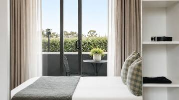 Habitación de hotel con cama, un pequeño balcón con mesa y silla, una planta en maceta y un zapatero.