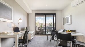 Un espace de bureau moderne comprenant un bureau, des chaises, un ordinateur et un téléphone. Une fenêtre offre une vue sur l’extérieur.