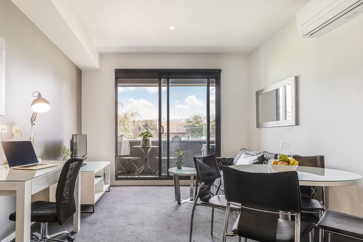 A modern office space with a desk, chairs, a computer, and a phone. There is a window with a view of the outdoors.