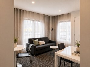 A hotel room with a sofa, two chairs, a small table, and a floor lamp. - Punthill Oakleigh (Hughesdale)