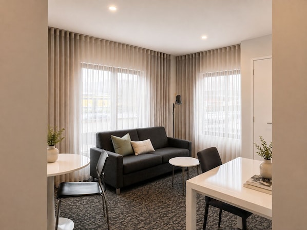 A hotel room with a sofa, two chairs, a small table, and a floor lamp.