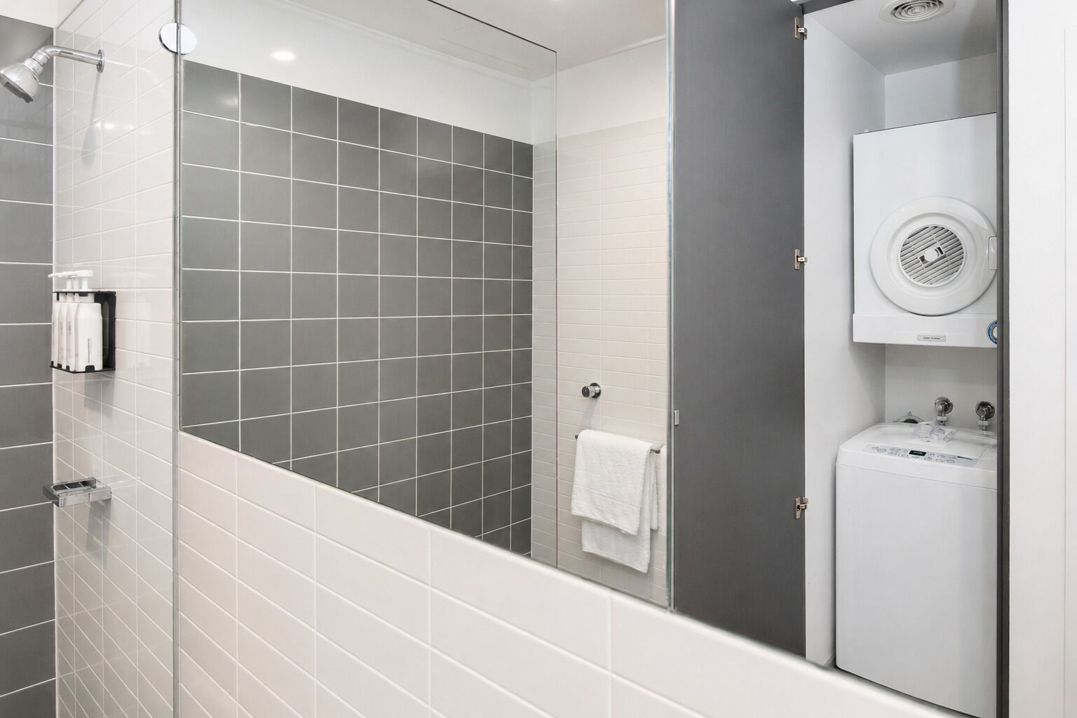 Un baño moderno con ducha, toallero y lavadora integrada.