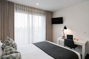 Une chambre d’hôtel avec un lit, un bureau avec un ordinateur, une télévision et une fenêtre avec des rideaux.