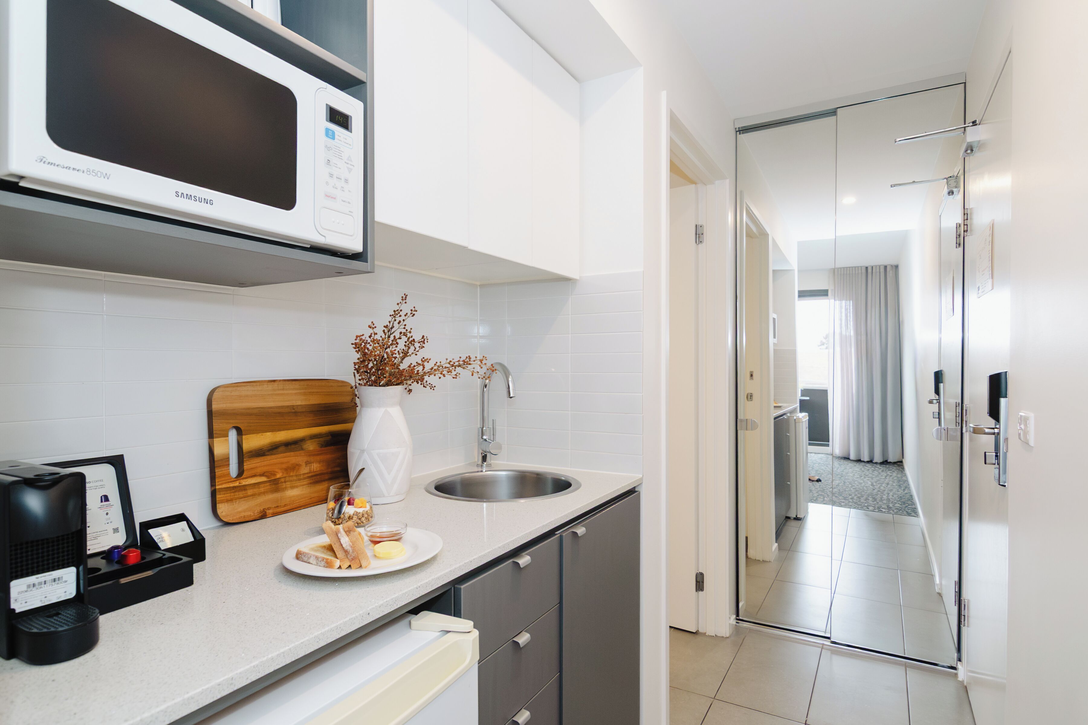 Eine moderne Küche mit Mikrowelle, Holzschneidebrett, Spüle und einer Arbeitsplatte mit Kaffeemaschine und einem Teller Essen.