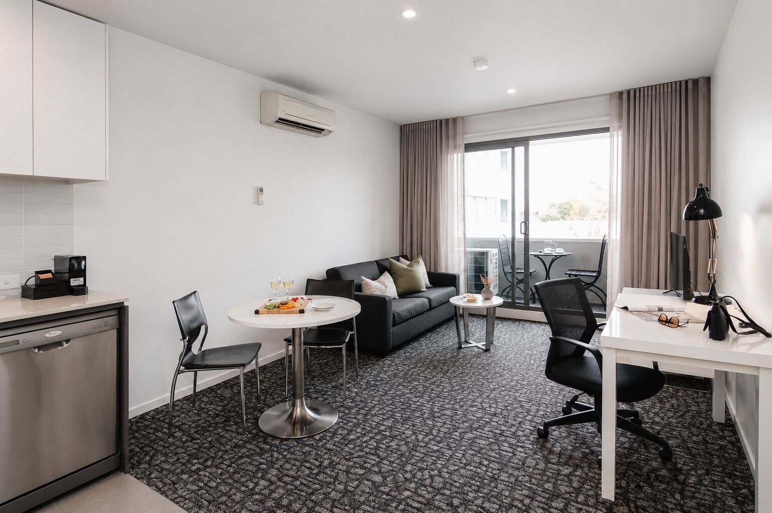 Ein modernes Hotelzimmer mit einer Küchenzeile, einem Essbereich mit Tisch und Stühlen, einer Couch und einem großen Fenster mit Vorhängen.