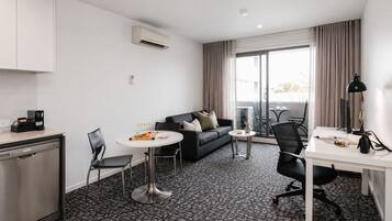 Ein modernes Hotelzimmer mit einer Küchenzeile, einem Essbereich mit Tisch und Stühlen, einer Couch und einem großen Fenster mit Vorhängen.