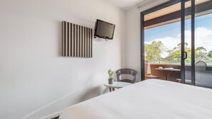 Une chambre d’hôtel avec un lit, un téléviseur fixé au mur, une petite table avec une plante et une chaise.