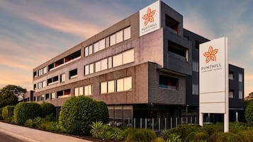 Un edificio de varios pisos con un diseño moderno, que presenta un logotipo destacado en la fachada y señalización que indica que es un hotel.