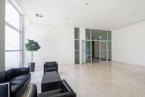 A spacious lobby with a large potted tree, black leather sofas, and a glass door leading to another area. - La Gioia Designers Lofts Luxury Apartments (Kraków)