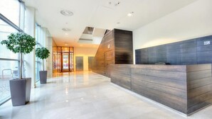 A modern reception area with a wooden reception desk, large windows, and potted plants. - La Gioia Designers Lofts Luxury Apartments (Kraków)