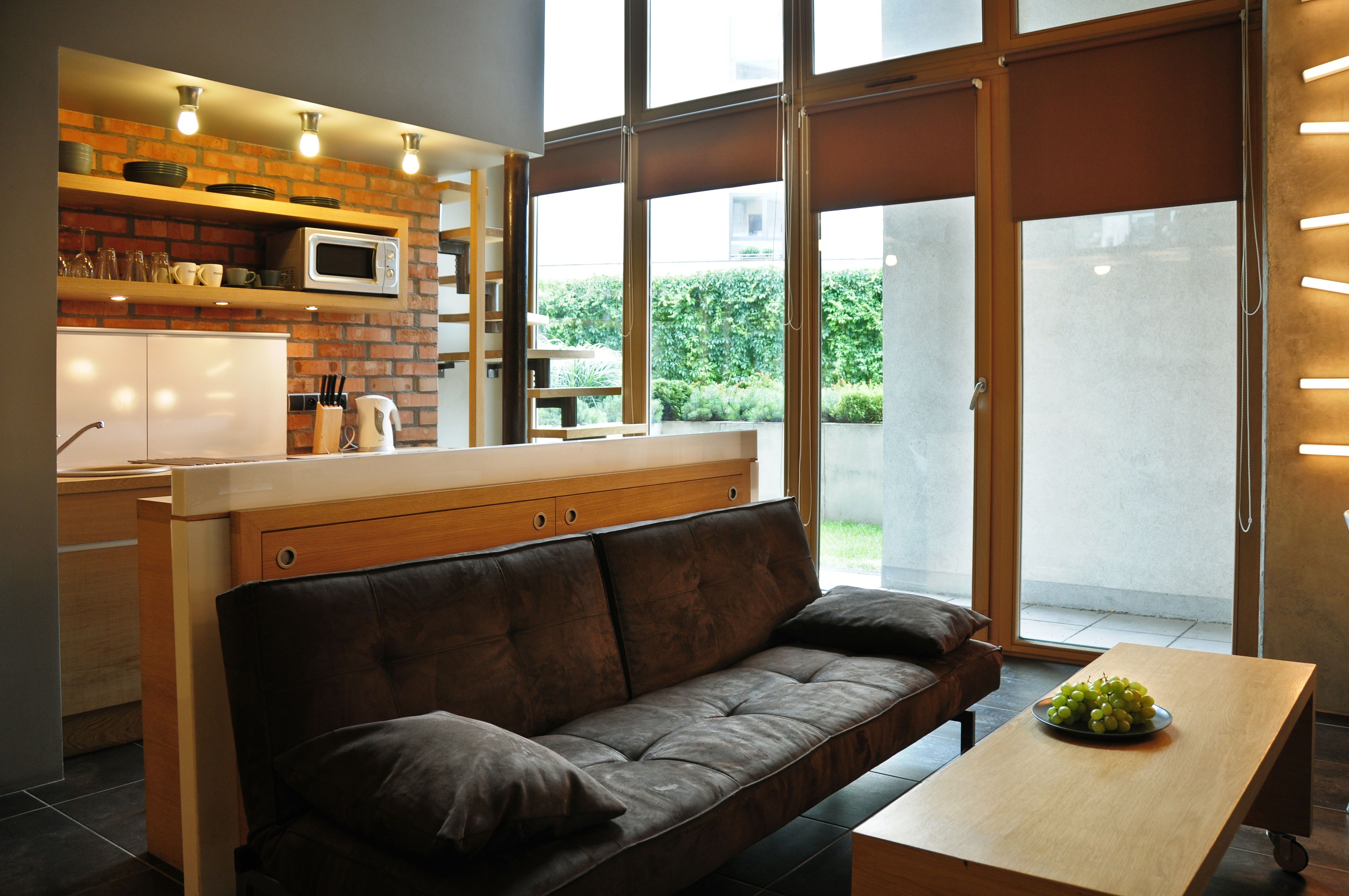 A modern kitchen with a microwave, shelves, and a window overlooking a garden.