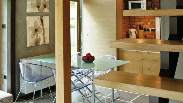 A modern kitchen with a microwave, wooden shelves, and a glass dining area with chairs. - La Gioia Designers Lofts Luxury Apartments (Kraków)