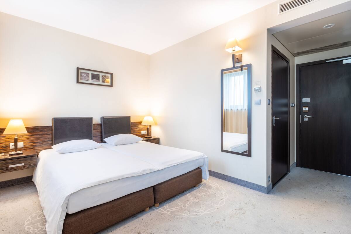 A hotel room with a large bed, two bedside lamps, a mirror, and a door.