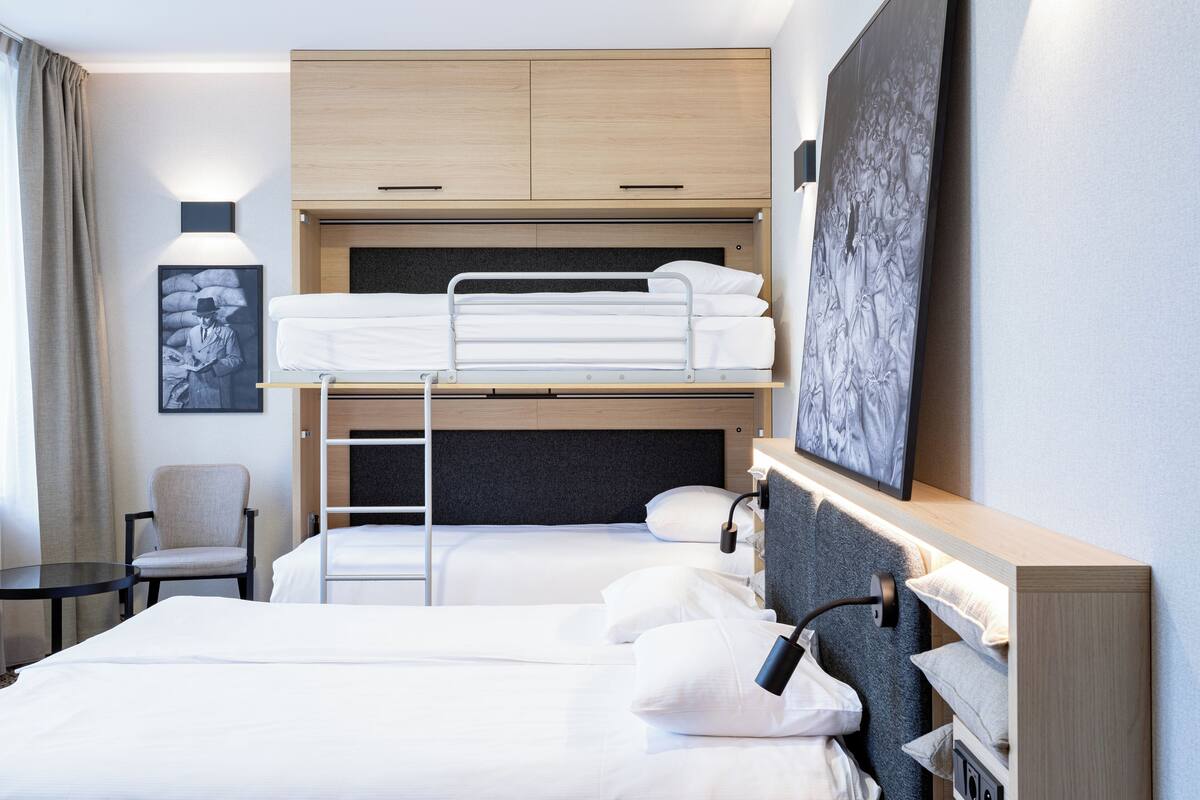 A hotel room with a bunk bed, a desk, a chair, and a painting on the wall.