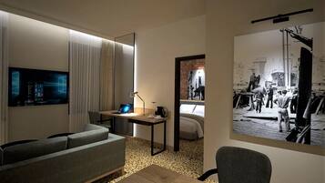 Una habitación de hotel moderna con un televisor grande, un escritorio con una computadora portátil, un sofá y una cama.