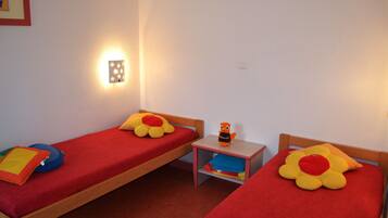 Une chambre avec deux lits simples, chacun recouvert d’une courtepointe rouge et agrémenté d’un oreiller en forme de fleur. Une table de chevet avec une lampe se trouve entre les deux lits.