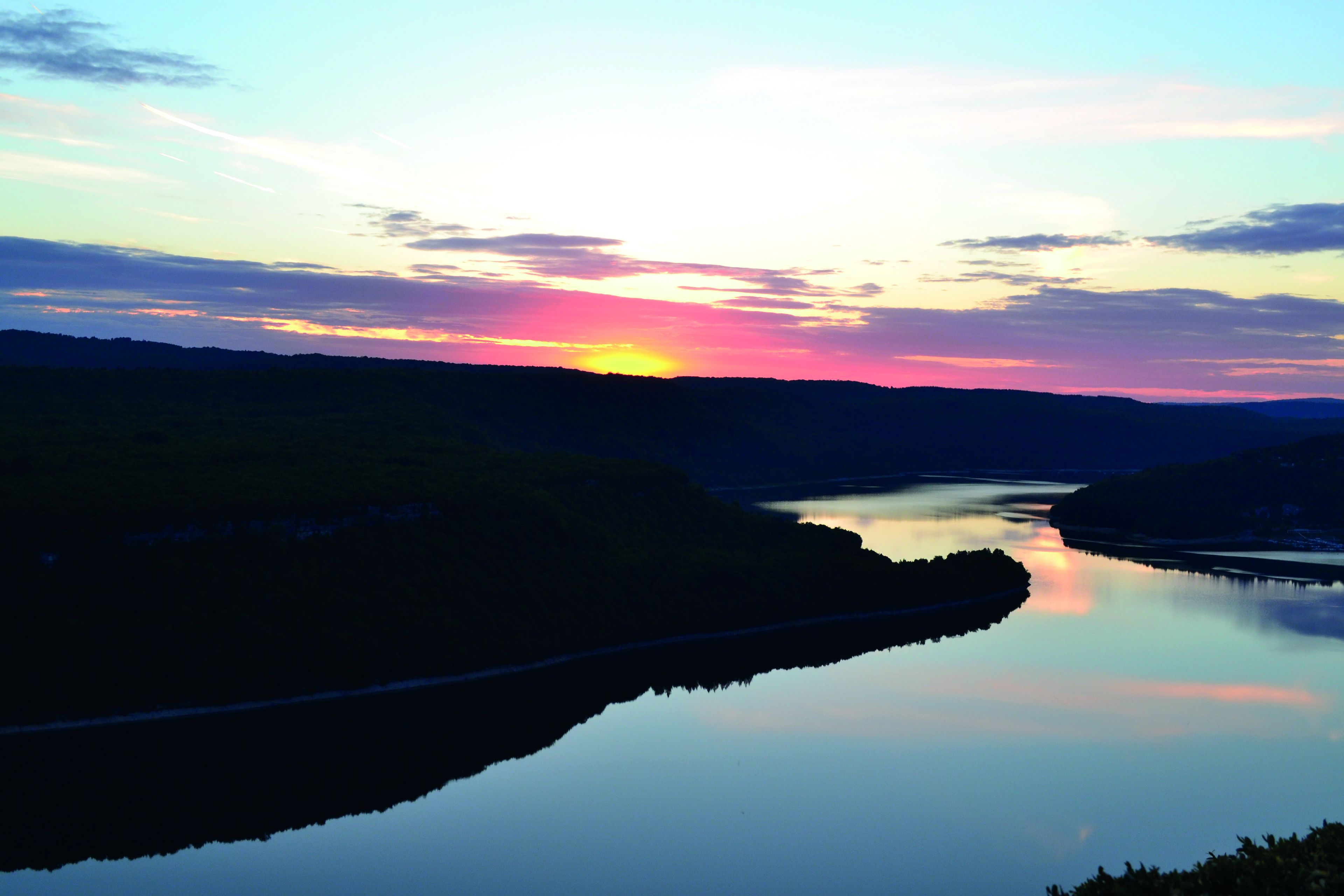 A calm river reflecting the sunset with hills in the background.