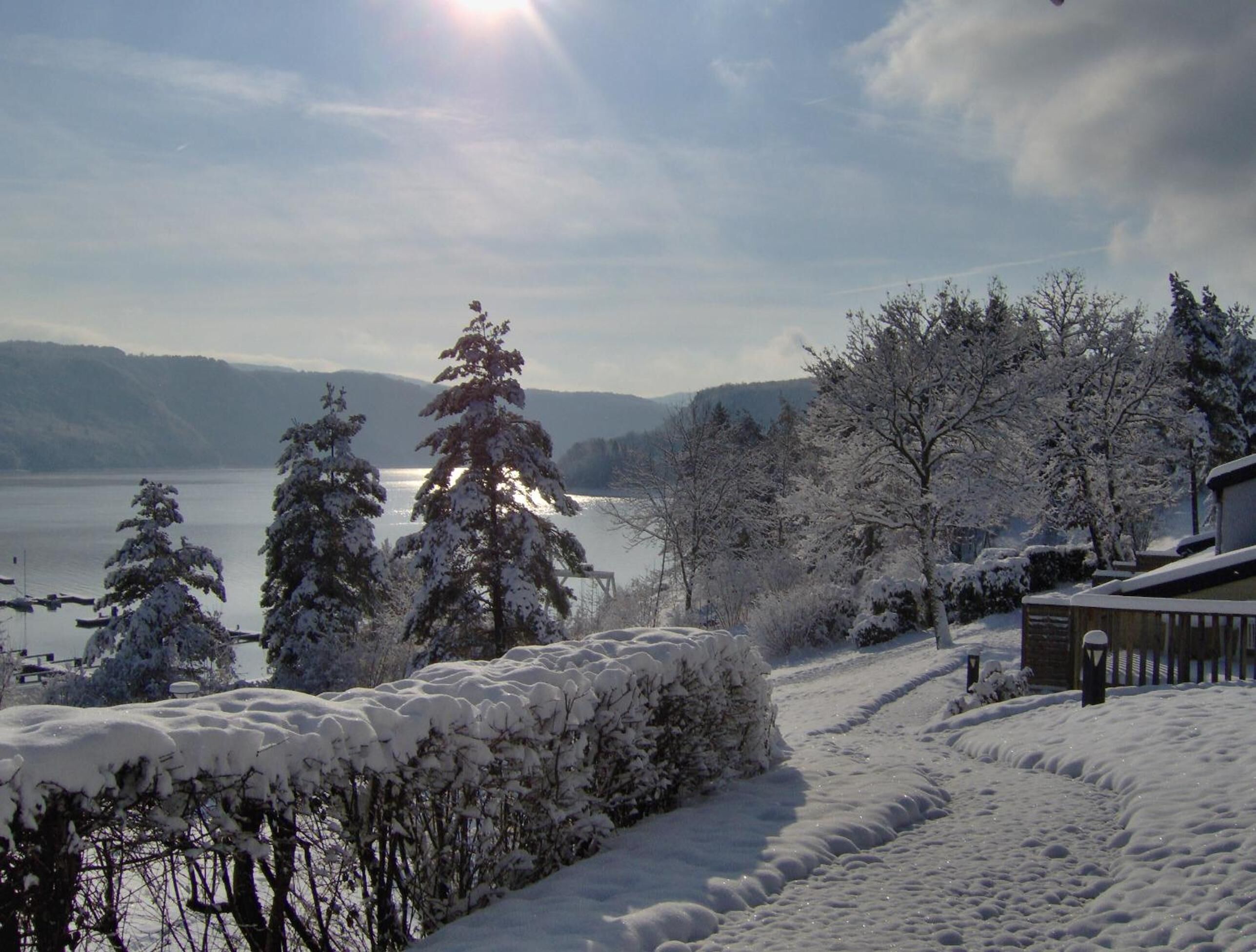 A snowy landscape with a lake, trees, and a house.