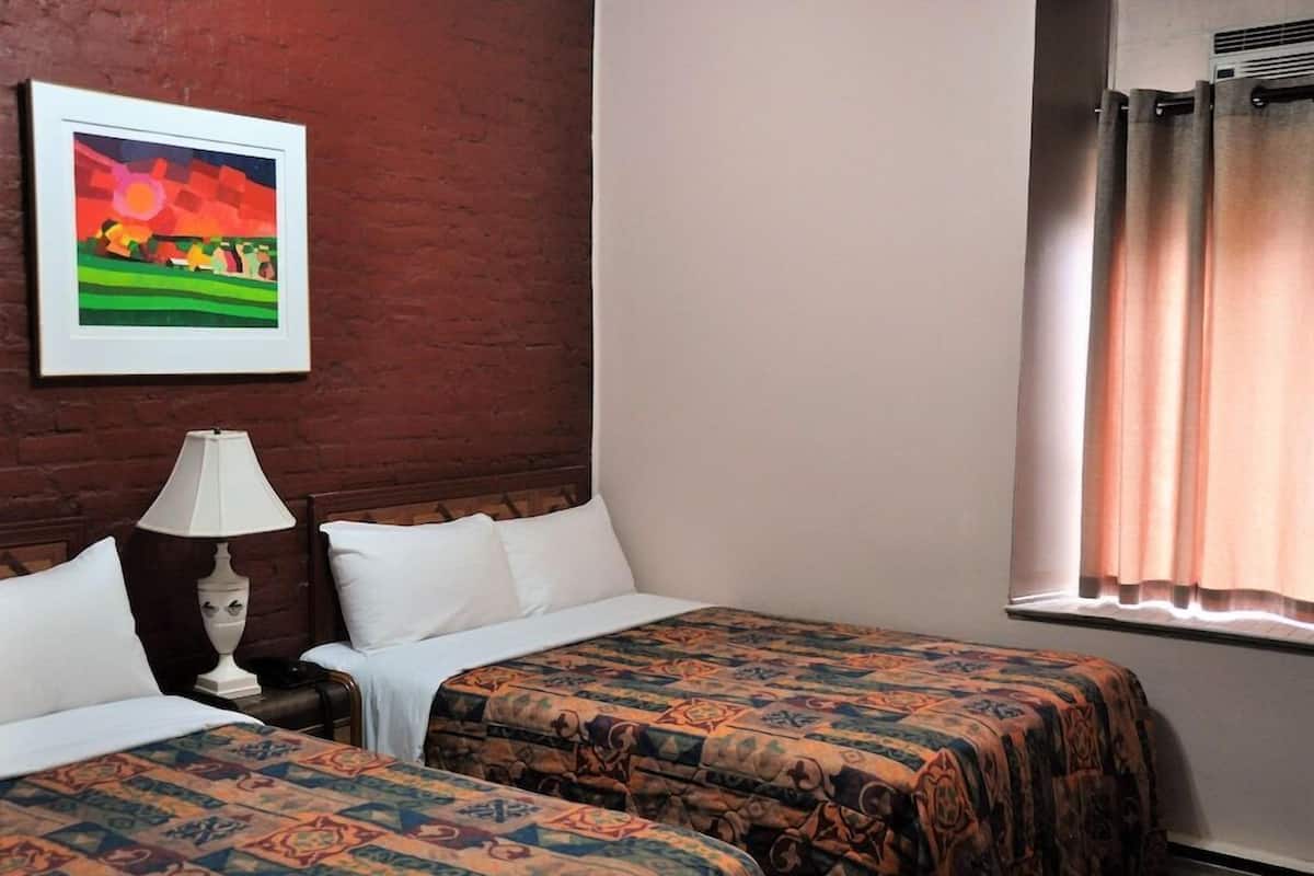 A hotel room with two beds, a nightstand, a lamp, a framed picture on the wall, and a window with curtains.