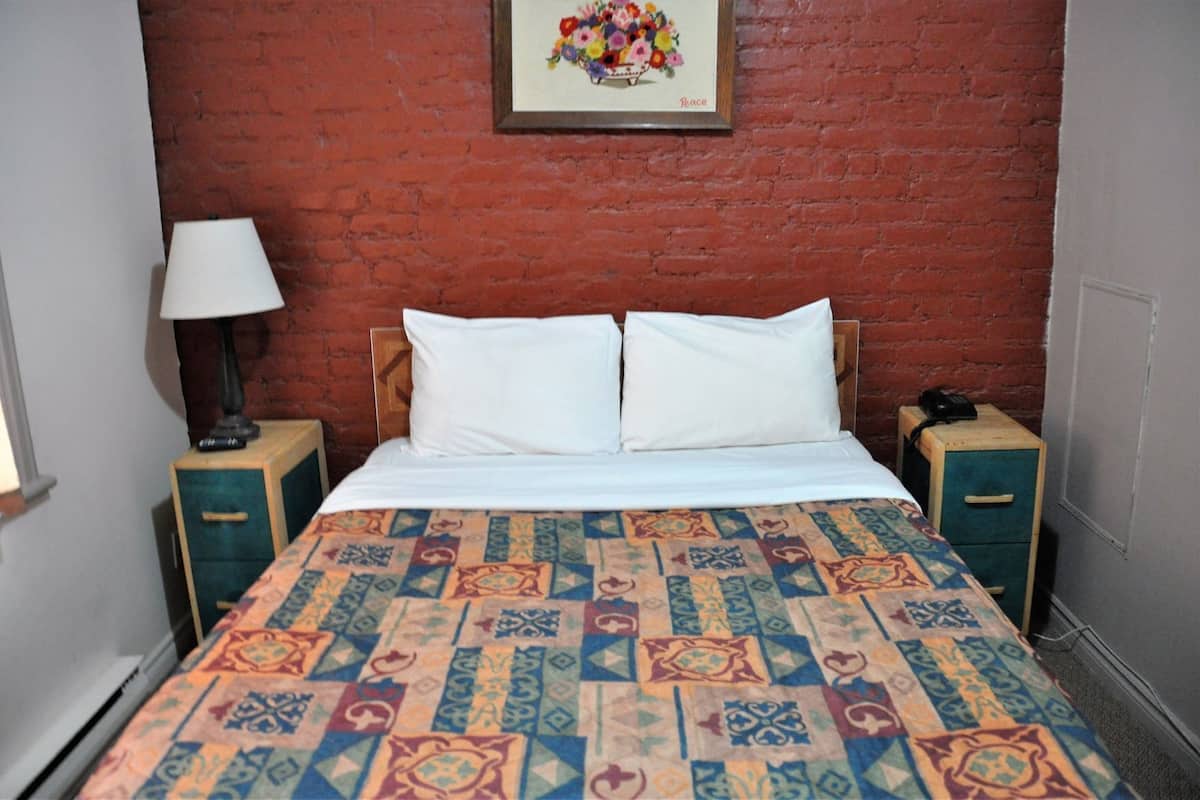 A bed with a patterned bedspread, two white pillows, a nightstand with a lamp, and a framed floral artwork on the wall.