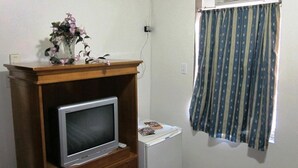 Um quarto pequeno com um móvel de madeira para televisão, uma geladeira branca, um ar-condicionado fixado na parede e uma cortina listrada.