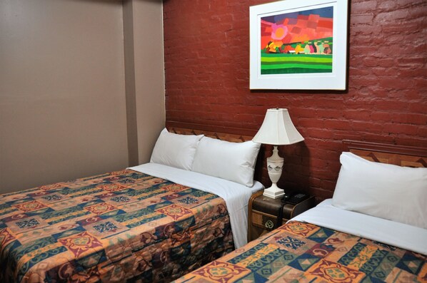 A hotel room with two beds, a nightstand with a lamp, and a colorful painting on the wall. - Hôtel Ste-Catherine (Montreal)