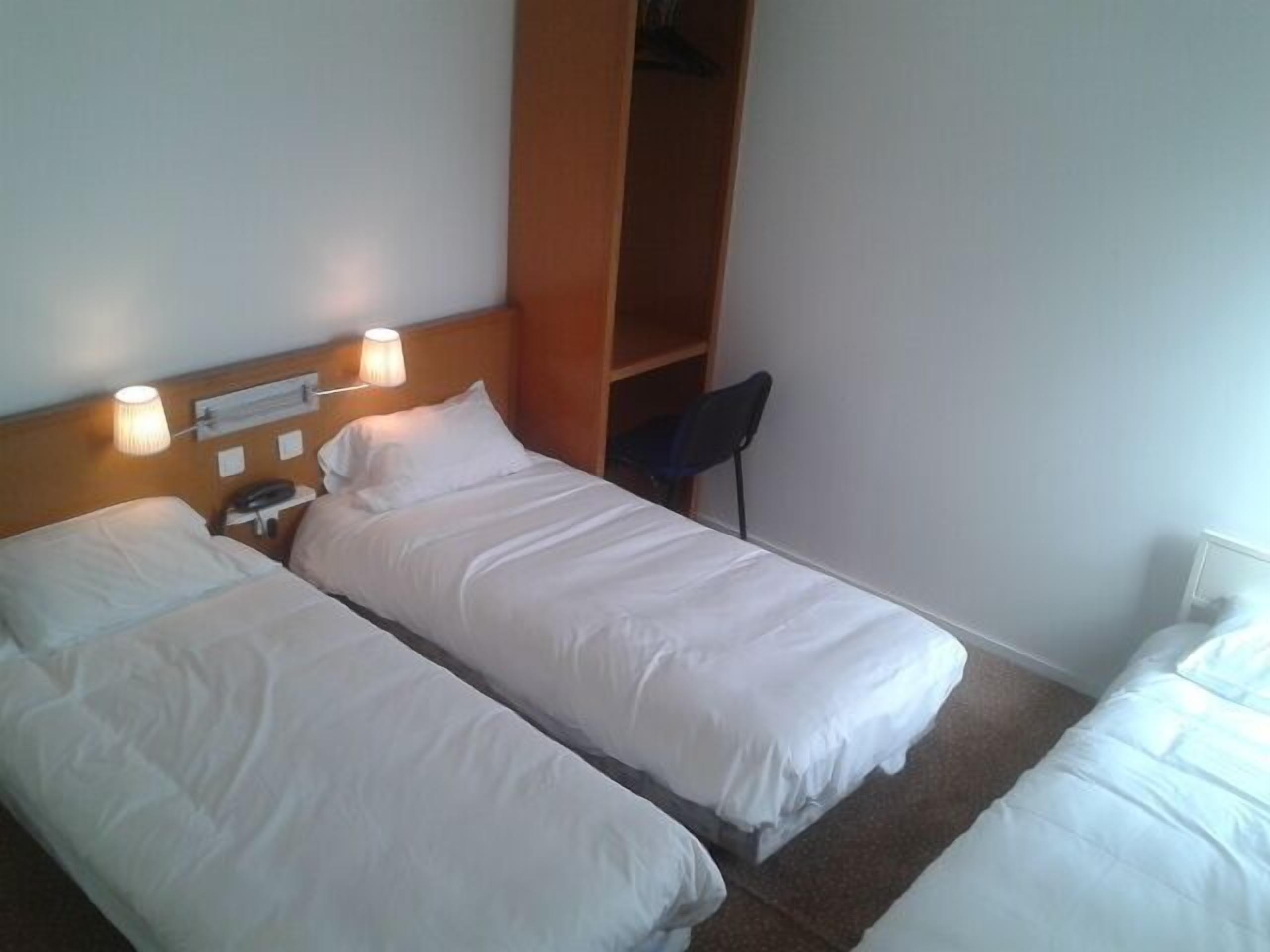 A hotel room with two single beds, a wooden headboard, a bedside lamp, and a small shelf.