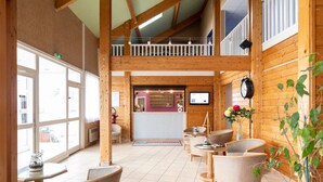 A wooden interior with a reception desk, seating area, and large windows.