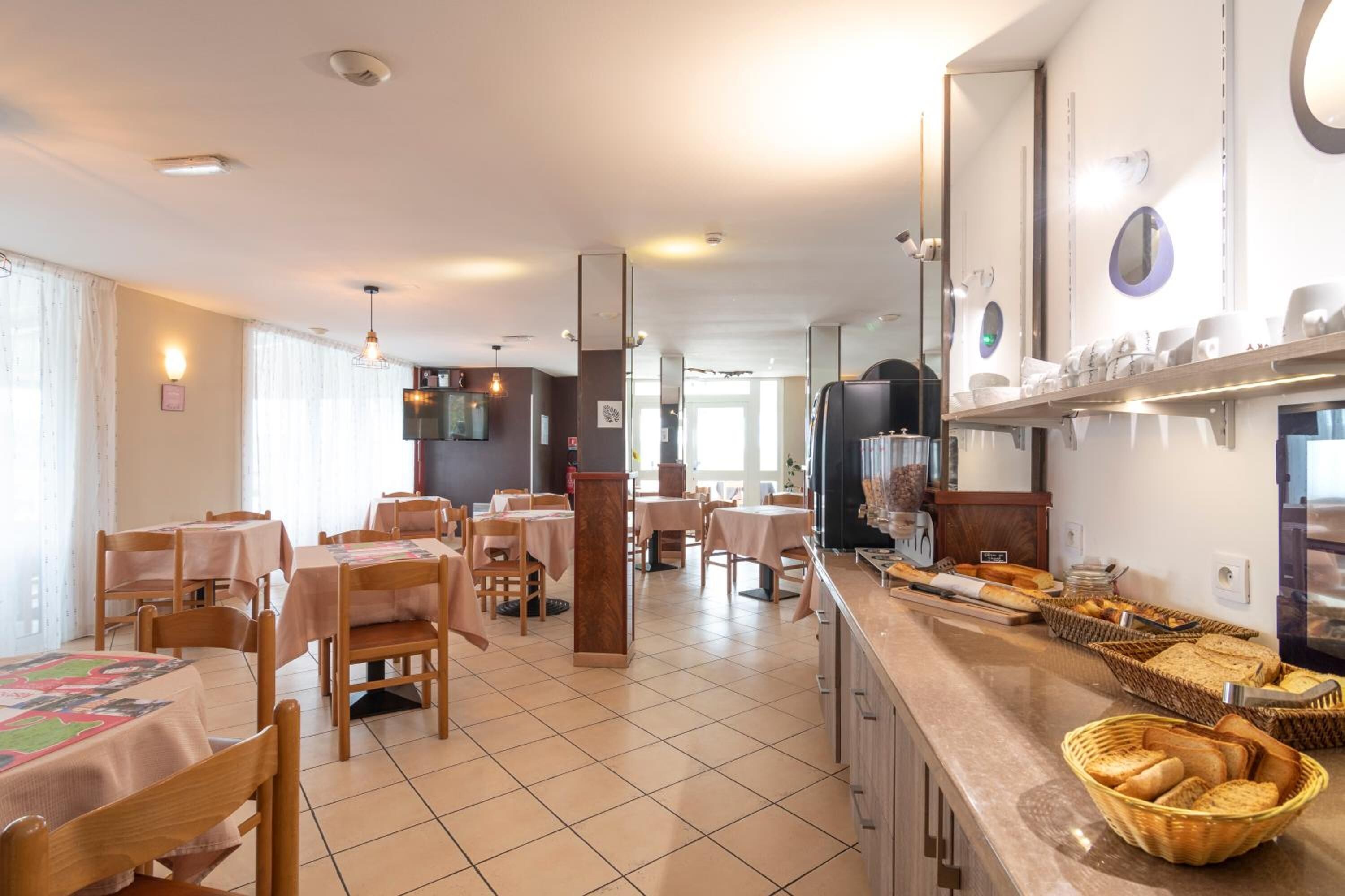 Un comedor con mesas y sillas, un mostrador de buffet con pan y bollería, y una pantalla de televisión.
