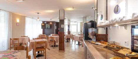 A dining area with tables and chairs, a buffet counter with bread and pastries, and a television screen.