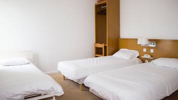 Habitación de hotel con dos camas individuales, un armario de madera, una silla y una mesita de noche con lámpara.