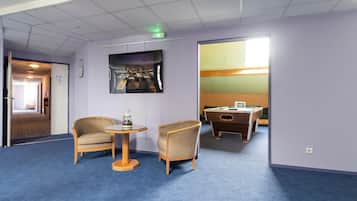 A room with a blue carpet, two wooden chairs, a small round table, a pool table, and a framed picture on the wall.