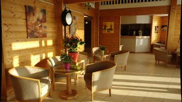 Una habitación acogedora con paredes de madera, una mesa redonda con sillas, un reloj y plantas en macetas.