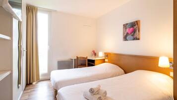 Habitación de hotel con dos camas, un escritorio, una silla, una ventana con cortinas y un cuadro en la pared.