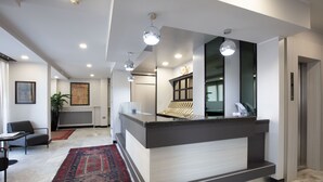 Un área de recepción con piso de mármol, un mostrador de recepción, un tapete grande, una planta y un cuadro en la pared.