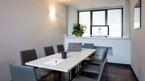 Una sala de reuniones moderna con una larga mesa, seis sillas, dos computadoras portátiles, una planta y un ventanal con un letrero que dice "HOTEL ESPERIA".