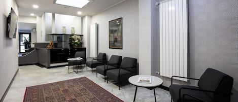 A modern living room with a large rug, black chairs, a small table, and a kitchen area in the background.
