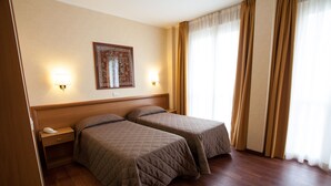 Habitación de hotel con dos camas, cabecero de madera, lámparas de noche, una mesita y un cuadro en la pared.