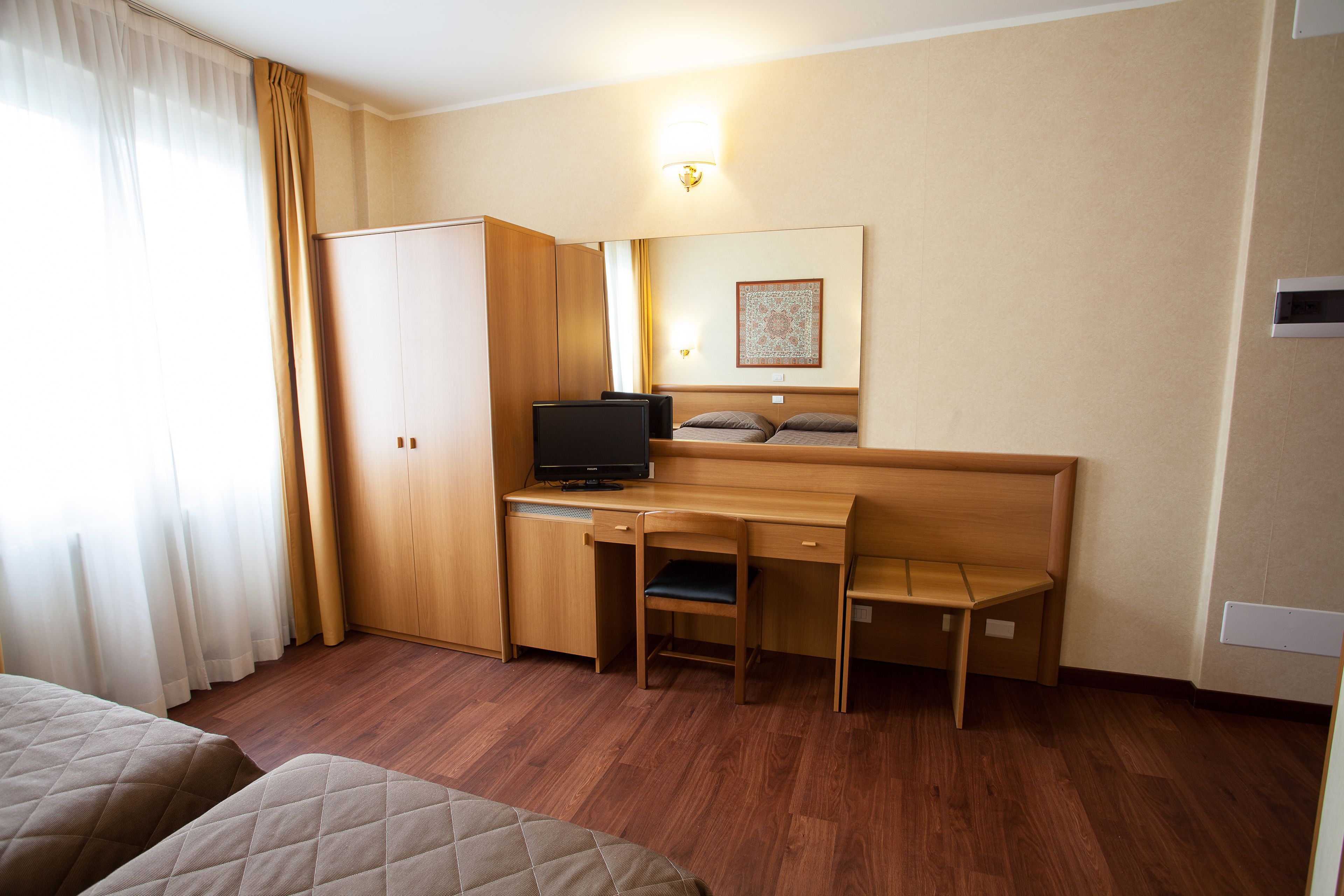 Una habitación de hotel con un escritorio de madera, un televisor, una cama y un armario.