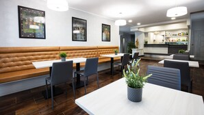 Un restaurante moderno con una zona de estar central que cuenta con un largo banco marrón y mesas blancas.